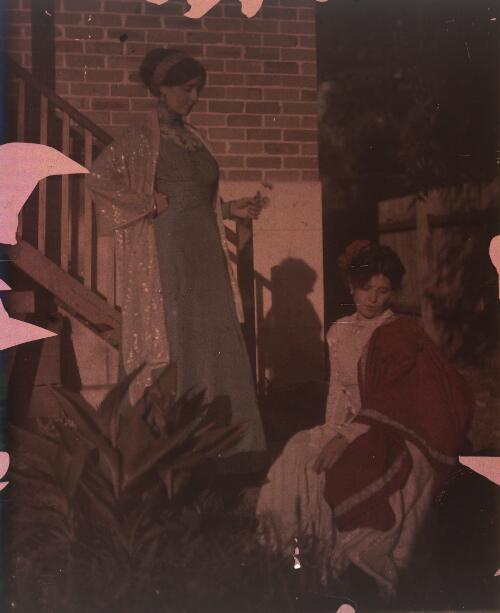 [Two unidentified women in garden with rear external staircase of house in background, ca. 1906] [transparency]