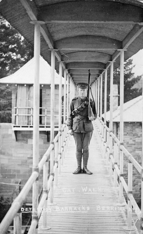 A camp guard standing at attention on the cat walk to the detention barracks, Berrima Internment Camp, New South Wales, approximately 1917 / D. Speer