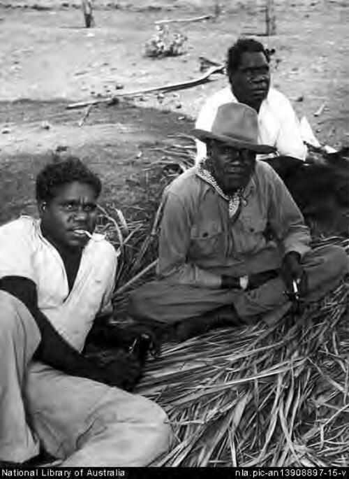 Three men sitting on palm fronds on the ground at the Mission Station, Cape York, North Queensland, 1957 [picture] / Wolfgang Sievers