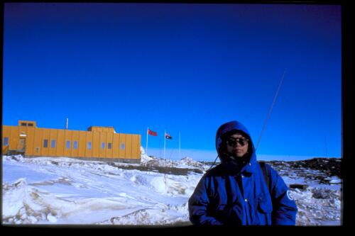 Dr Wu Bin, station doctor at Zhong Shan, stands before the Australian and Chinese flags raised when another nation is on base, Davis Station, Antarctica, November 1997 [transparency] / Felicity Jenkins