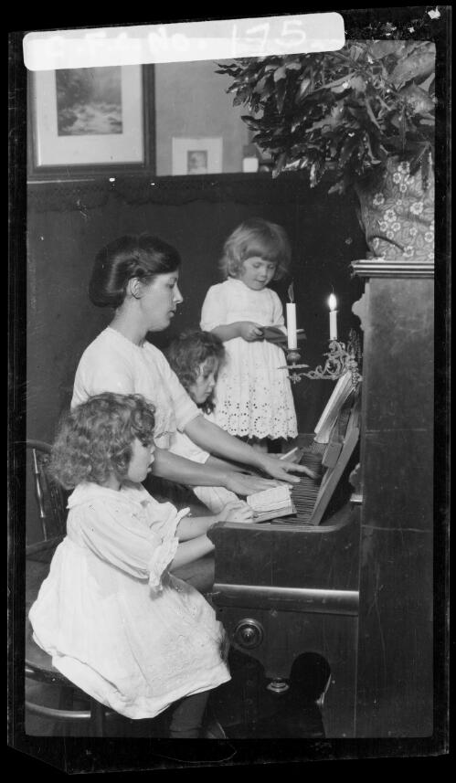 Winifred Cazneaux playing piano with Rainbow, Jean and Beryl, 1914? [picture] / Harold Cazneaux