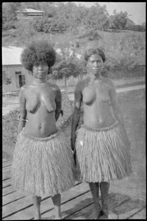 Two Papuan women wearing grass skirts standing on a jetty, Papua, ca. 1923 [picture] / Sarah Chinnery