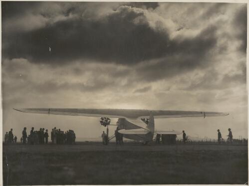 Rear view of Avro Ten monoplane, Faith in Australia, VH-UXX, with small crowd gathered at left and cyclists at right, 1930s [picture]