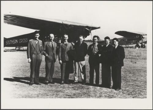Group portrait of Charles Kingsford-Smith, third from left, and his partners standing in front of Fokker F.VIIb/3m, Southern Cross, on left, and Avro 618 Ten, Faith in Australia, Mascot Aerodrome, Sydney, ca. 1933 [picture]