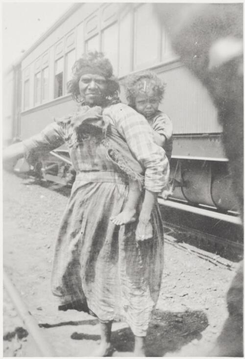 Aboriginal woman standing beside a railway line and carrying a child on her back, Wynbring, South Australia, 1921 [picture]
