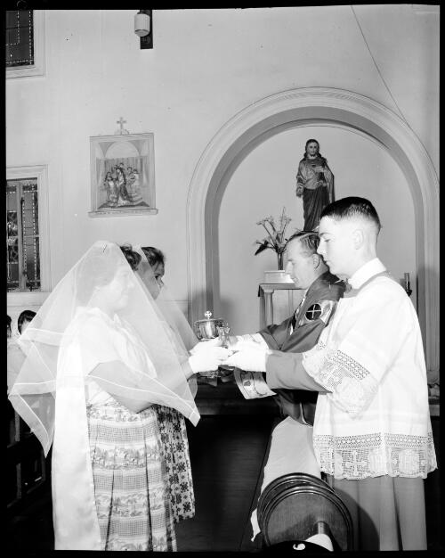 A priest with an altar boy serving first communion to a two Home of the Good Shepherd girls' home girls during mass in the chapel, Ashfield, 8 October, 1963 [picture] / John Mulligan
