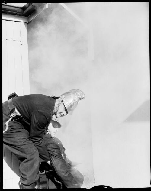 A fireman dragging another fireman out of a smoky building during training, Sydney, 25 June, 1962 [picture] / John Mulligan