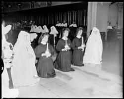 Postulants and professed nuns kneeling before the bishop during a ...