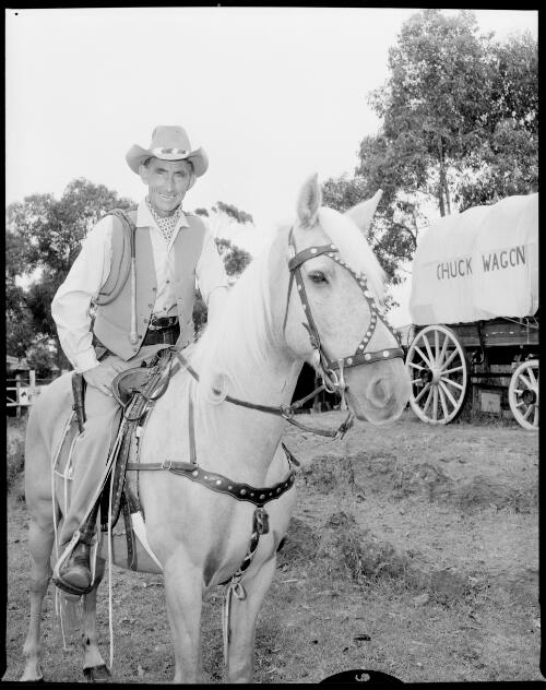 Close up of Smoky Dawson on his horse Flash with a chuck wagon in the background, Mona Vale road, Terrey Hills, New South Wales, 1 March, 1968 [picture] / John Mulligan