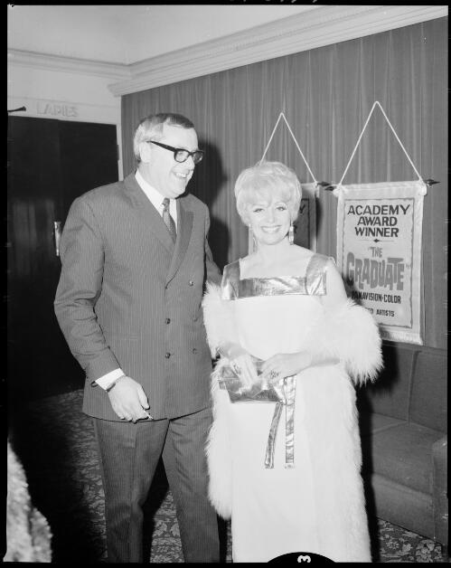 An unidentified man and woman standing in front of some banners at the premiere of The graduate, Hoyts Mayfair Theatre, Sydney, 28 July, 1968 [1] [picture] / John Mulligan