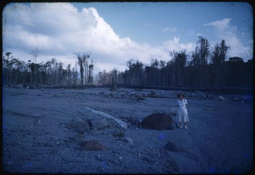 Sister Gilbert at the Andemba River, standing by a large, hot rock deposited by the volcano overnight, Papua New Guinea, 1951 [transparency] / Albert Speer