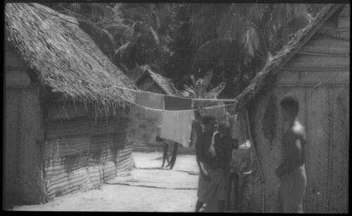 Houses with man and a woman holding a baby Carteret Islands, Papua New Guinea, 1960 [picture] / Terence and Margaret Spencer