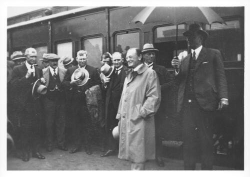 [Portrait of Leopold Amery, Secretary of State for Dominion Affairs, standing under an umbrella surrounded by a group of people at a railway station during his visit to Australia, 1927-1928] [picture]