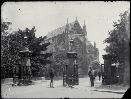 [Entrance to The Domain with three unidentified people and view of St. Mary's Roman Catholic Cathedral in background, Sydney] [picture] / Robert Morse Withycombe