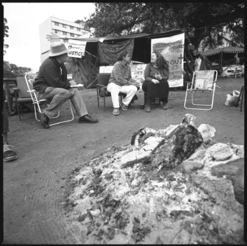 [Bonny Briggs, Corrie and other] people sitting and standing around the sacred fire, Aboriginal Tent Embassy, Victoria Park, University of Sydney, 19 August 2000 [picture] / Loui Seselja