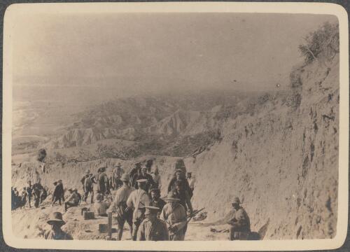 First refugees [climb up the hillside on foot from inland Turkey partly accompanied by soldiers and file past a dozen or so Anzac soldiers standing at the top of the trail or seated nearby, May? 1915] [picture] / J.P. Campbell