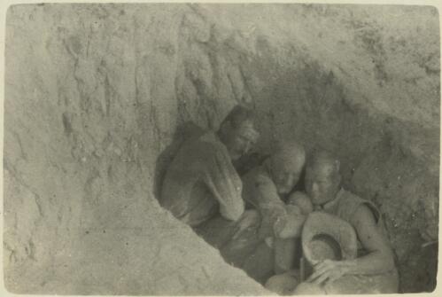 Sheltering from bursting shells, [showing three Anzac soldiers huddled together sheltering in a shallow trench, June? 1915] [picture] / J.P. Campbell