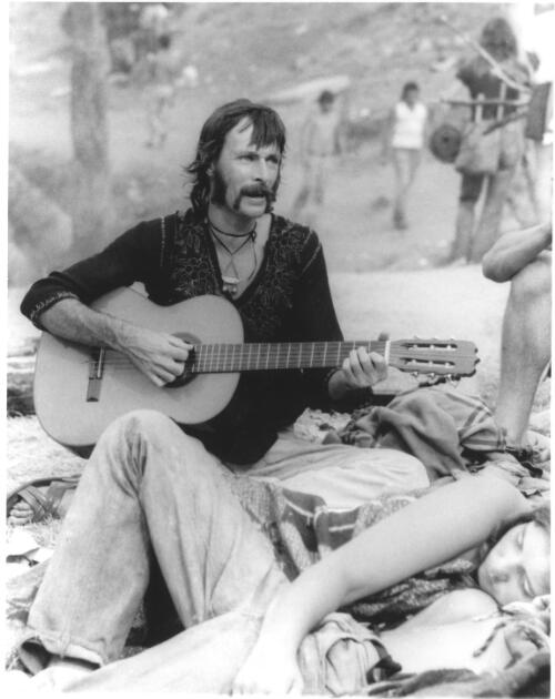 A more mature man singing and playing guitar while others cuddle and listen, Sunbury 1972 [picture] / Soc Hedditch