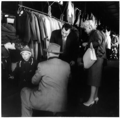 Trying on a coat at a second-hand clothing stall, Queen Victoria Markets, Melbourne, 1956 [picture] / Jeff Carter