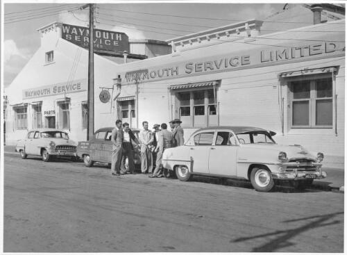 A group of unidentified men stand conversing next to the survey car outside Waymouth Service Limited after the Ampol Trial survey team arrive in Adelaide, April, 1956 [picture]