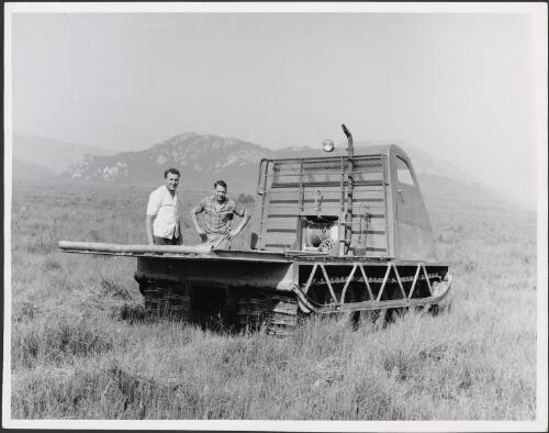 Bombardier driver, Stan Reynolds, on right with another man standing beside the Bombardier on track to Serpentine River, Hydro-Electric Commission expedition by Bombardier to the Serpentine River, Tasmania, 1961 [picture] / Russ Ashton