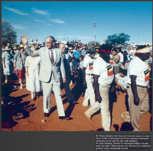 Sir Ninian Stephen, the Governor-General, waves to some of the 4,000 crowd gathered for the Handover/Leaseback Ceremony, as he and his wife, Lady Stephen, Mr. Clyde Holding, Minister for Aboriginal Affairs, his wife, Judy, and other official guests are escorted by traditional owners to the ceremonial mound [picture] / prepared by Media and Communications, Department of Aboriginal Affairs