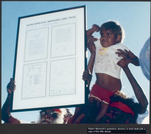 Nipper Winmarti's grandson, Benson, is held aloft with a copy of the title deeds [picture] / prepared by Media and Communications, Department of Aboriginal Affairs