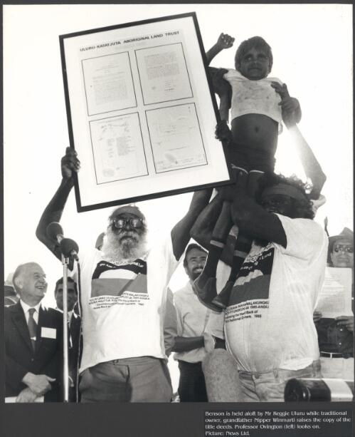 Vincent Nipper is held aloft by Mr. Reggie Uluru, while one of the Anangu traditional owners, his grandfather Nipper Winmati, raises the title deeds with Professor Ovington looking on [picture] / News Ltd