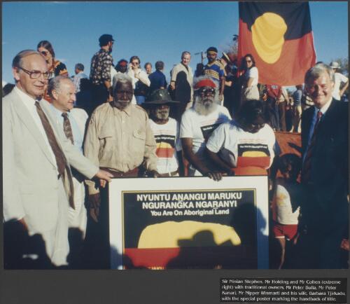 Sir Ninian Stephen, Mr. Holding and Mr. Cohen (extreme right) with traditional owners, Mr. Peter Bulla, Mr. Peter Kanari, Mr. Nipper Winmarti and his wife, Barbara Tjirkadu, with the special poster marking the handback of title [picture] / prepared by Media and Communications, Department of Aboriginal Affairs