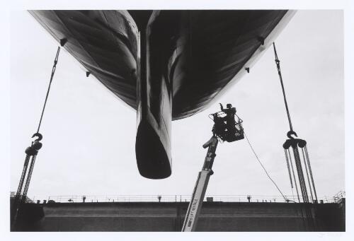 Spray-painters use a hydraulic hoist to paint anti-foul on the underside of the vessel's stern, seen here with the rudder removed at the Captain Cook Graving Dock, Garden Island, New South Wales, 2001 [picture] / Jon Reid