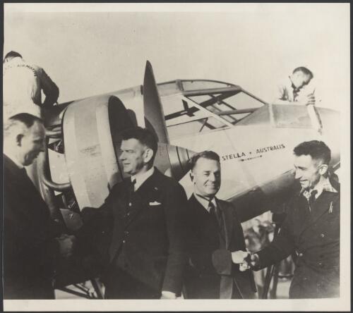 Charles Ulm and J. L. Skilling being farewelled in front of Stella Australis plane VH-UXY by American officials, Oakland Aerodrome, California, United States, 3 December 1934 [picture]
