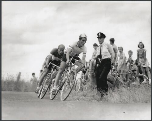 Riders in the road race make a turn watched by young spectators and a policeman near Broadmeadows, Victoria, 1956 [picture] / Bruce Howard