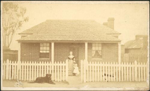 A woman and infant outside brick house with picket fence, Hill End, New South Wales, ca. 1873 [picture] / Beaufoy Merlin