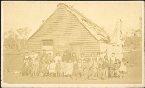 Man and group of children outside weatherboard building with bark roof, Gulgong, New South Wales, ca. 1872 [picture]
