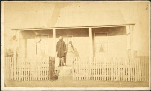 Presbyterian minister Thomas Starr [?] and his wife on the veranda of their cottage with corrugated iron roof and paling fence, Hill End, New South Wales, ca. 1872 [1] [picture]