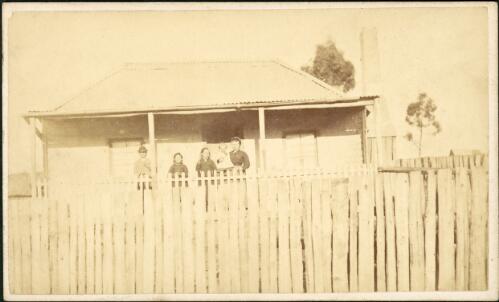 Mother and four children on verandah of rendered cottage with corrugated iron roof and paling fence, Hill End, New South Wales, ca. 1872 [1] [picture]