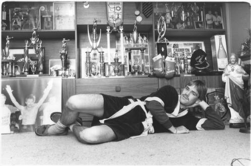 Lester Ellis lays on the floor in front of a wall full of trophies he collected during his boxing career 1986 [picture] / Bruce Howard