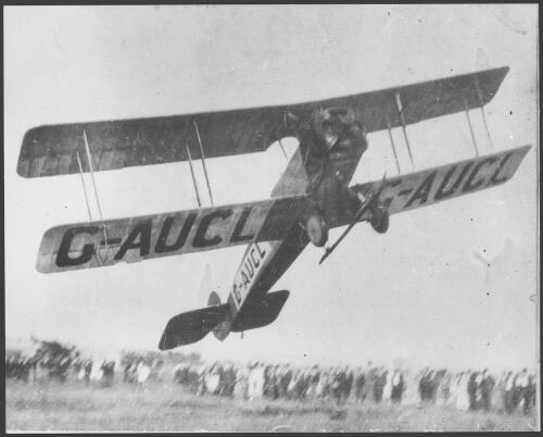 Avro 504J biplane G-AUCL in flight crosses the finish line in a race with crowd in background, 1926 [picture]