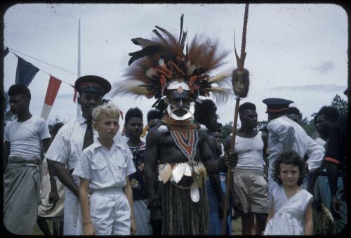 Highland native wearing bird of paradise plumes at Wabag, government appointed headmen wearing red banded caps in the background, between 1955 and 1960 [transparency] / Tom Meigan