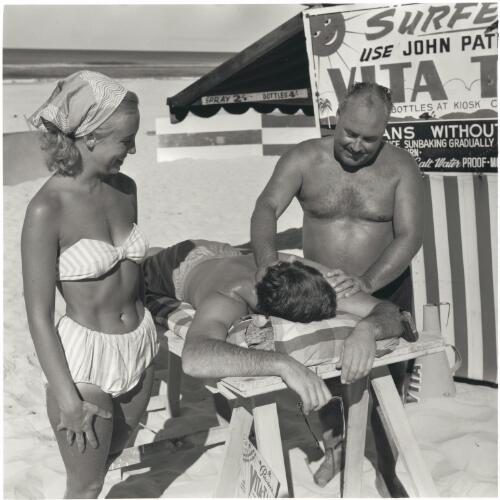 John Paterson applies 'Vita Tan' to a customer at his booth on the Gold Coast, 1957 [picture] / Jeff Carter