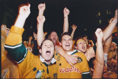 Three friends in the crowd at the Rocks watching the last minutes of the live telecast of the Rugby World Cup final in 2003, Australia lost the final in the last minute, [1] [picture] / Ben Rushton