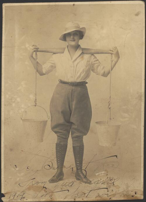 [Portrait of Vera Pearce carrying two buckets, one on either side, hanging by ropes from a rod across her shoulders, 1919] [picture] / Langham