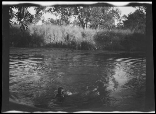 One of the expedition team, nicknamed Joker, with a fish between his teeth swimming in Montejinni Waterhole, Northern Territory, 1925 / Michael Terry