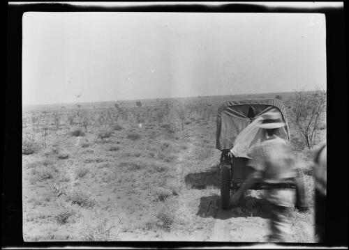 Expedition member walking past a Guy roadless truck with trailer parked on a sand dune, Western Australia, 1925 / Michael Terry