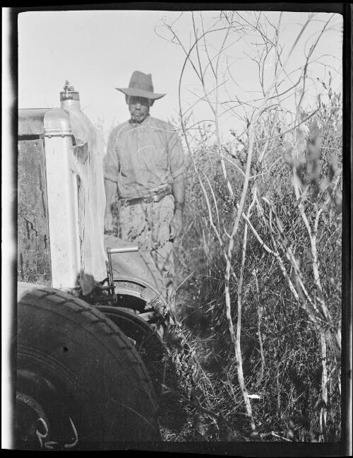 Tom Campbell standing at the front of a vehicle in dense wattle scrub inland from Wallal, Western Australia, 1928 / Michael Terry