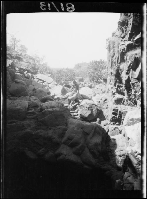 Expedition member and his dog sitting at the entrance of a rock pool, Tanami region, Northern Territory, 1929 / Michael Terry