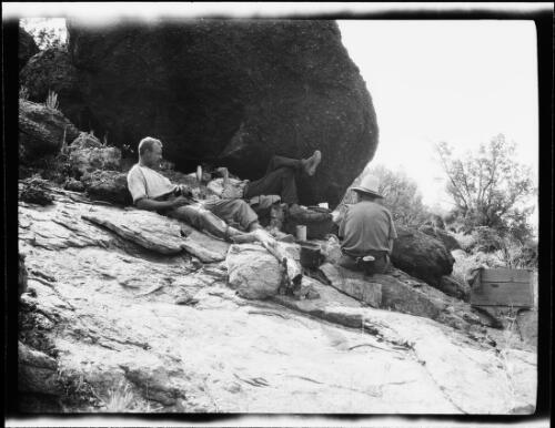 Michael Terry and two expedition members resting in the shade of a large boulder near the Pottoyu Hills in the Petermann Ranges, Northern Territory, 1930