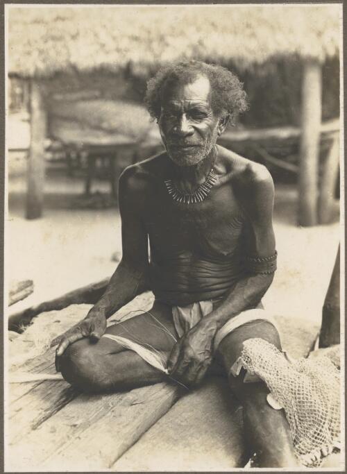 Men of Mailu [elderly man sitting on wooden deck rolling fibrous material on his thigh] [picture] / Frank Hurley