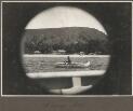Murray Island [view through a port hole of a man in a boat on water and a village in background] [picture] / Frank Hurley