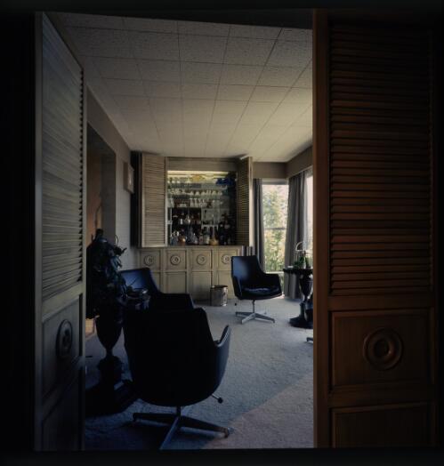 [Room with a bar fitment with a mirror behind the bottles and glasses next to chrome based, vinyl covered swivel chairs, ca. 1971] [transparency] / David Beal